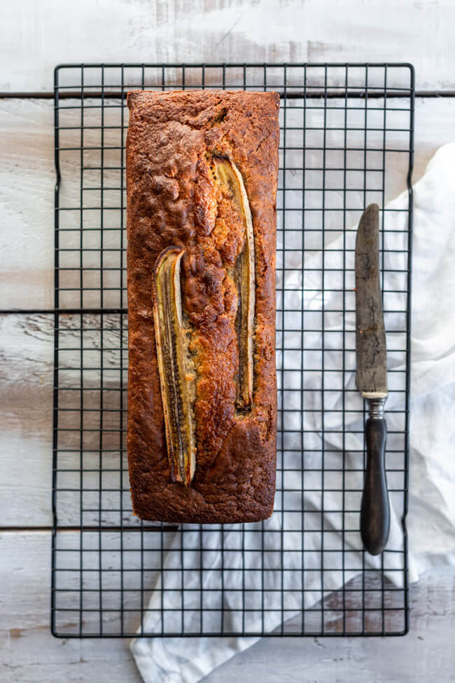 Bananenbrot mit Schokolade auf schwarzem Kuchnrost mit altem Messer.