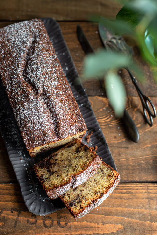 Bananenbrot mit Schokolade auf schwarzer Kuchenplatte.