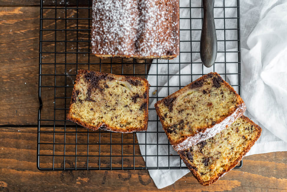 Bananenbrot mit Schokolade auf schwarzem Kuchnrost mit altem Messer.