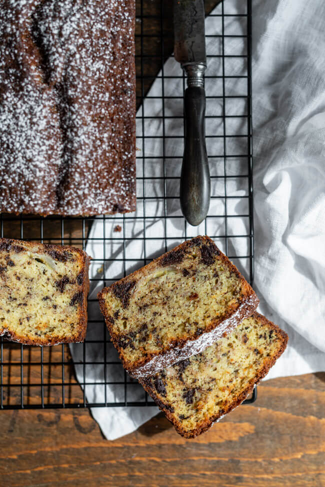 Bananenbrot mit Schokolade auf schwarzem Kuchnrost mit altem Messer.