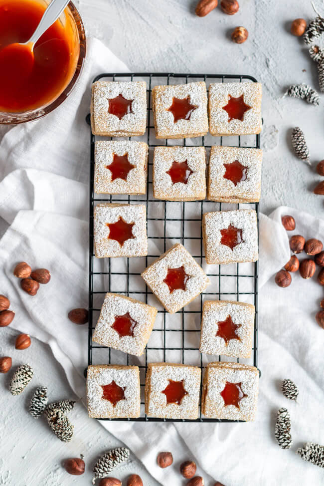 Köstliche Weihnachtsplätzchen: Haselnuss-Spitzbuben mit Hiffenmark auf schwarzem Metallgitter.