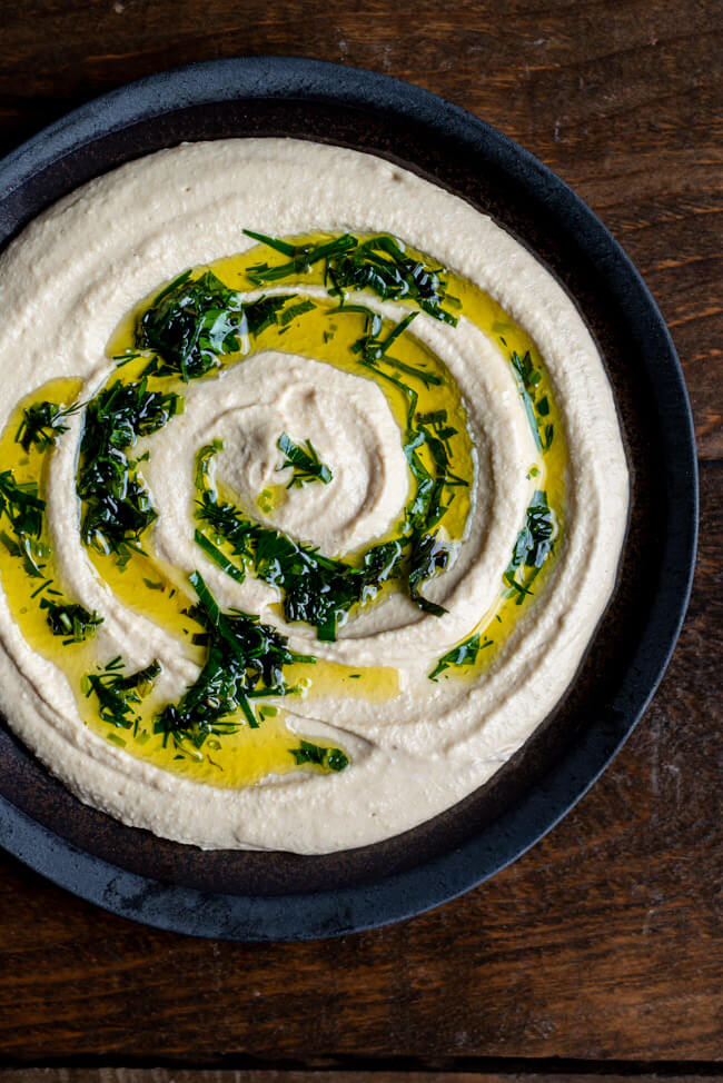 Weltbester Hummus mit Kräuteröl auf dunklem Keramikteller zum International Hummus Day.