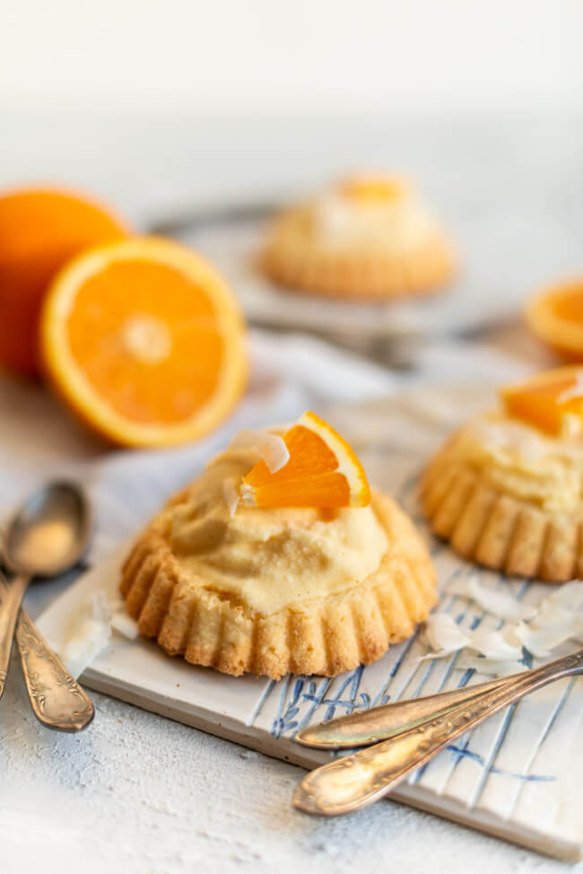 Eistörtchen mit Orangeneis und Kokosrapseln auf Keramikbrettchen.