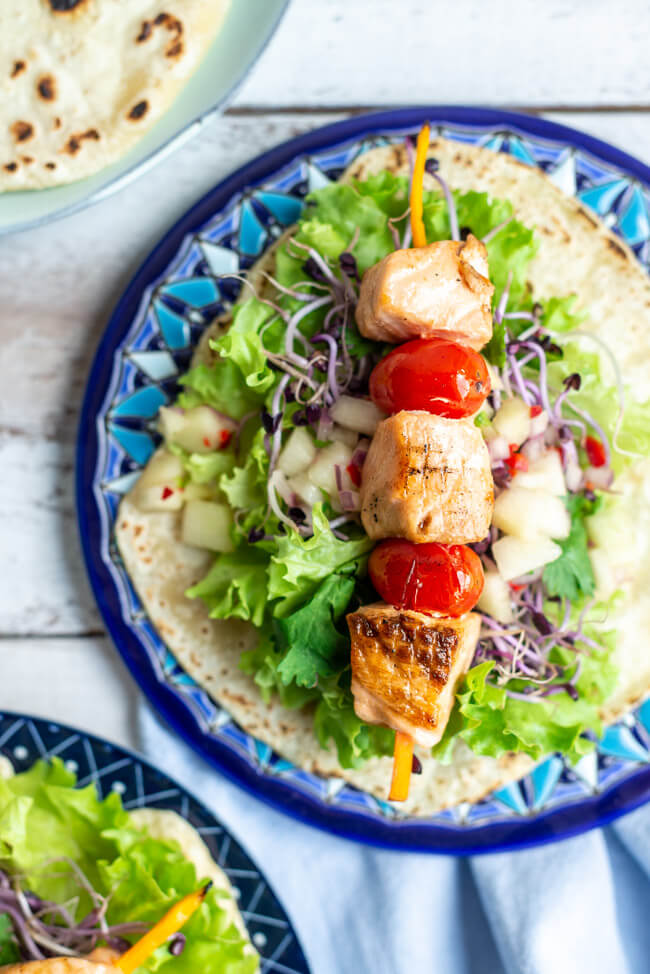 Lachs Tacos mit Melonen-Salsa auf blauen Keramiktellern und weißem Holztisch.