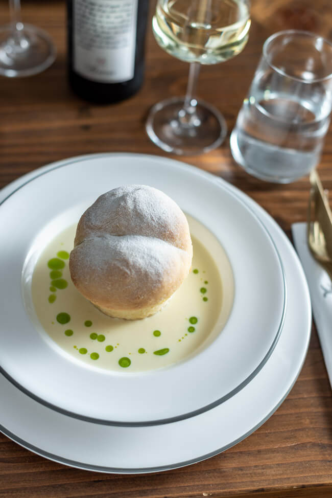 Gefüllte Buchteln mit karamellisierten Zwiebeln mit Bergkäse-Sauce und Schnittlauchöl auf weißem Keramikteller.