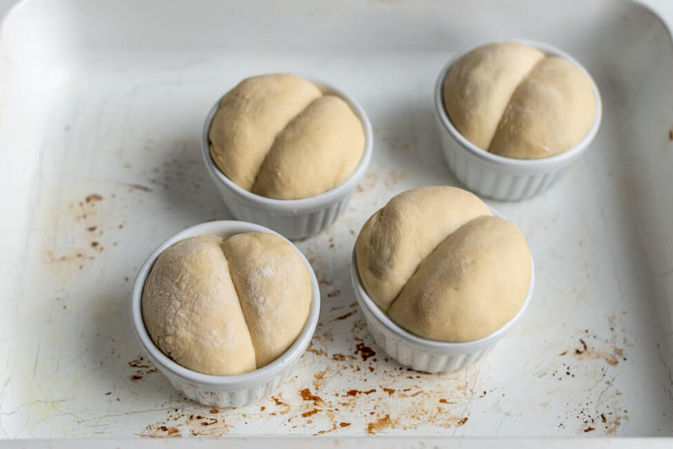 Buchteln mit karamellisierten Zwiebeln in weißen Keramiktöpfchen.