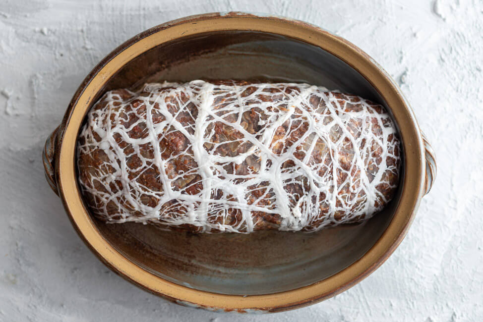 Weihnachtlicher Hackbraten im Schweinenetz in der Auflaufform, vor dem Backen.