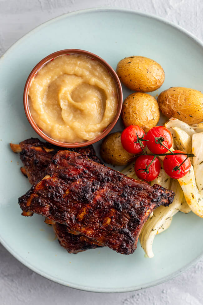 Mediterrane Rippchen mit Ofengemüse und Knoblauchsauce auf blauem Keramikteller.