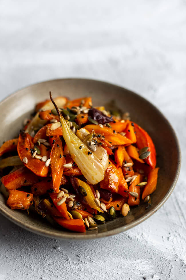 Veganer winterlicher Salat aus geröstetem Wurzelgemüse mit Saaten und Schwarzkümmel in grauen Keramikteller auf hellem Untergrund.