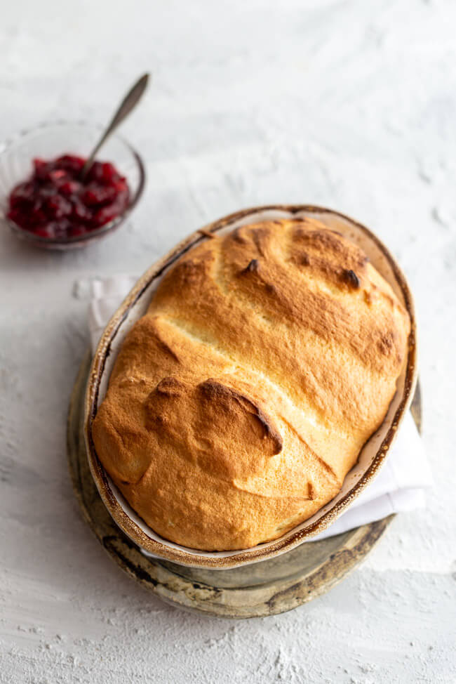 Salzburger Nockerl aus Kitchen Impossible in Auflaufform auf hellem Untergrund mit Schale Cranberry Kompott.