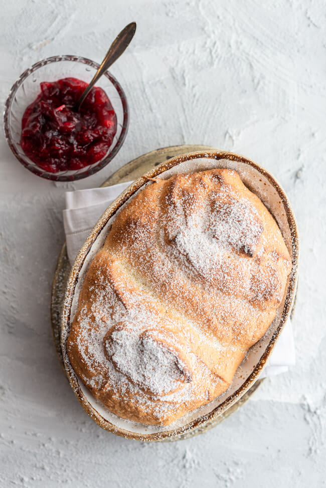 Salzburger Nockerl mit Puderzucker bestäubt aus Kitchen Impossible in Auflaufform auf hellem Untergrund mit Schale Cranberry Kompott.