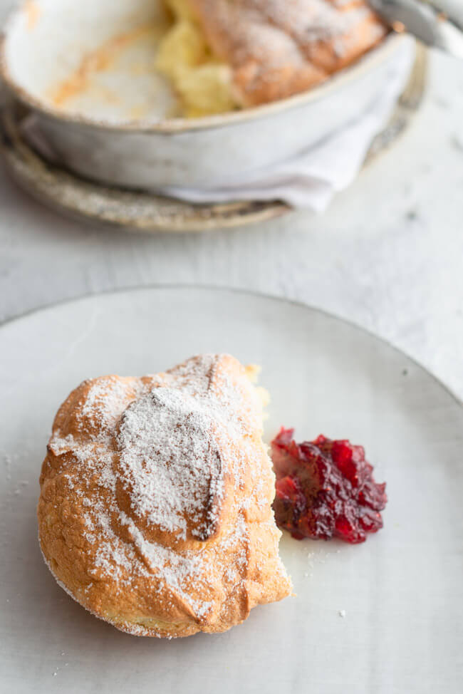Salzburger Nockerl mit Puderzucker bestäubt aus Kitchen Impossible auf rauem Keramikteller auf hellem Untergrund mit einem Kleks Cranberry Kompott.
