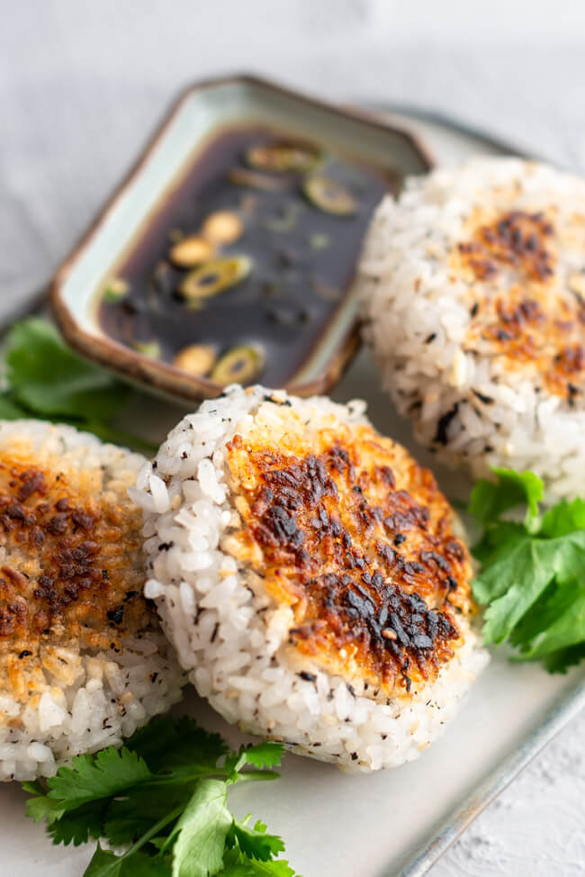 Onigiri gefüllt mit Erdnüssen, Frühlingszwiebeln und Knoblauch auf weißem Keramikteller mit japanischem Dip aus Sojasauce und Essig.