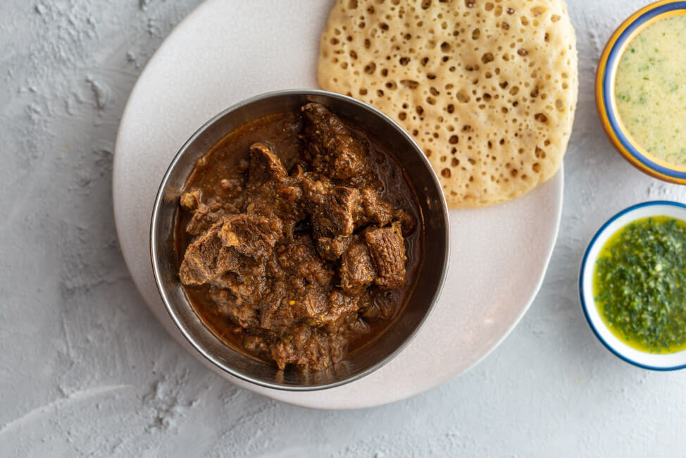 Jemenitischer Rindfleisch-Eintopf mit Sauerrahm und Koriander, serviert in Schale, dazu Lachuch und zwei Dips: Hilbeh und Zhug, aus Kitchen Impossible.
