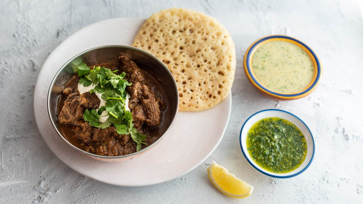 Jemenitischer Rindfleisch-Eintopf mit Sauerrahm und Koriander, serviert in Schale, dazu Lachuch und zwei Dips: Hilbeh und Zhug, aus Kitchen Impossible.