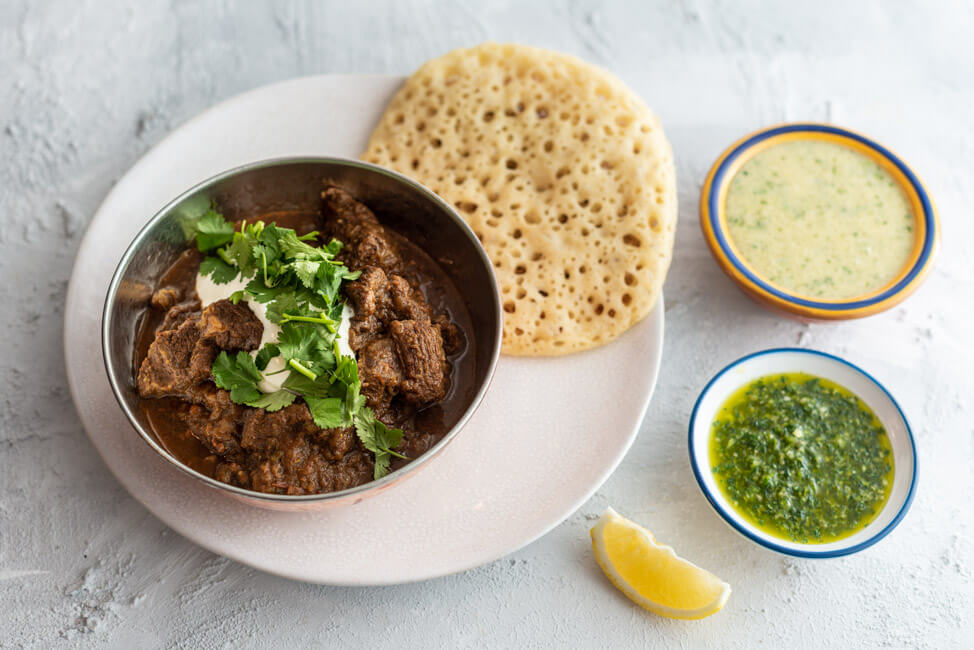 Jemenitischer Rindfleisch-Eintopf mit Sauerrahm und Koriander, serviert in Schale, dazu Lachuch und zwei Dips: Hilbeh und Zhug, aus Kitchen Impossible.
