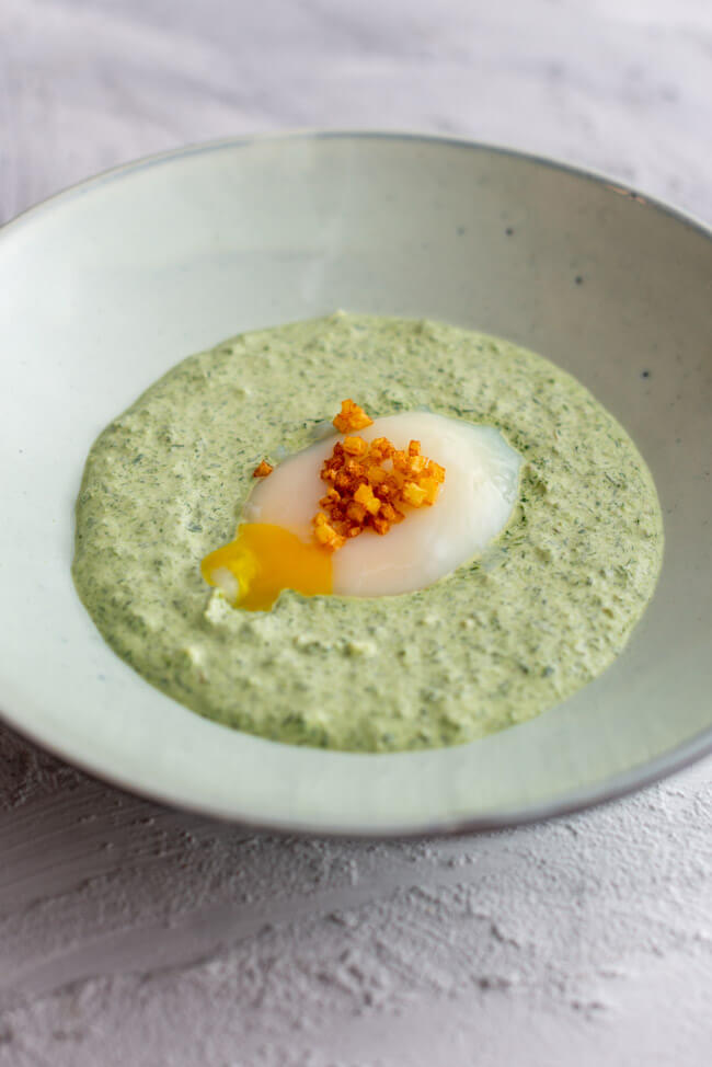 Rezept von Mario Lohninger aus Kitchen Impossible: Frankfurter Grüne Soße mit 60-Minuten-Ei und Kartoffel-Brunoises in hellblauem Teller und hellem Untergrund.