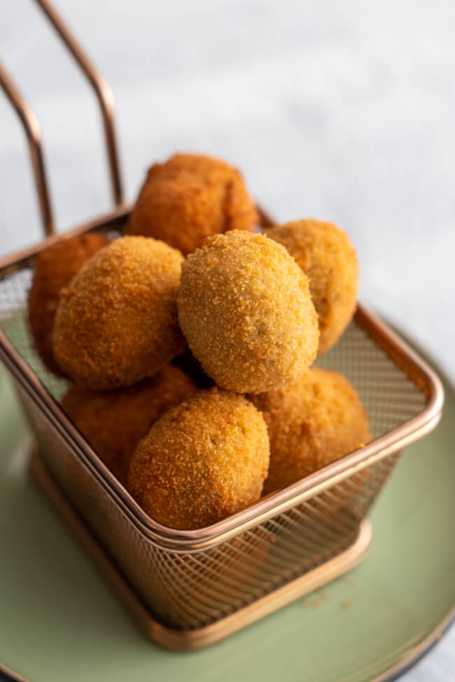 Originalrezept aus Kitchen Impossible: Olive Ascolane des Piceno - gefüllte und panierte Oliven in goldenem Körbchen auf hellem Untergrund.