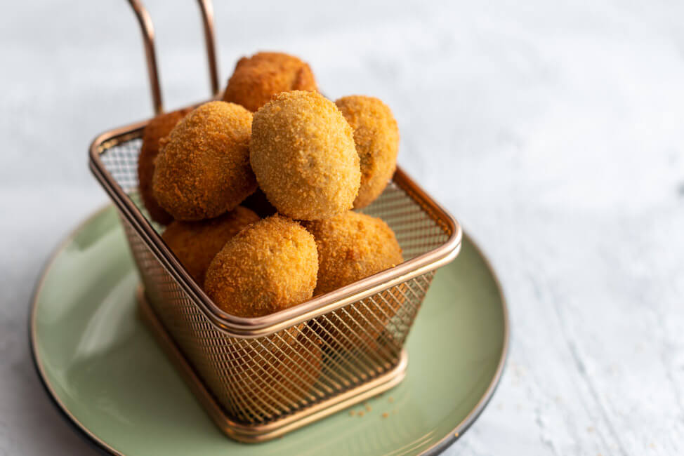 Originalrezept aus Kitchen Impossible: Olive Ascolane des Piceno - gefüllte und panierte Oliven in goldenem Körbchen auf hellem Untergrund.