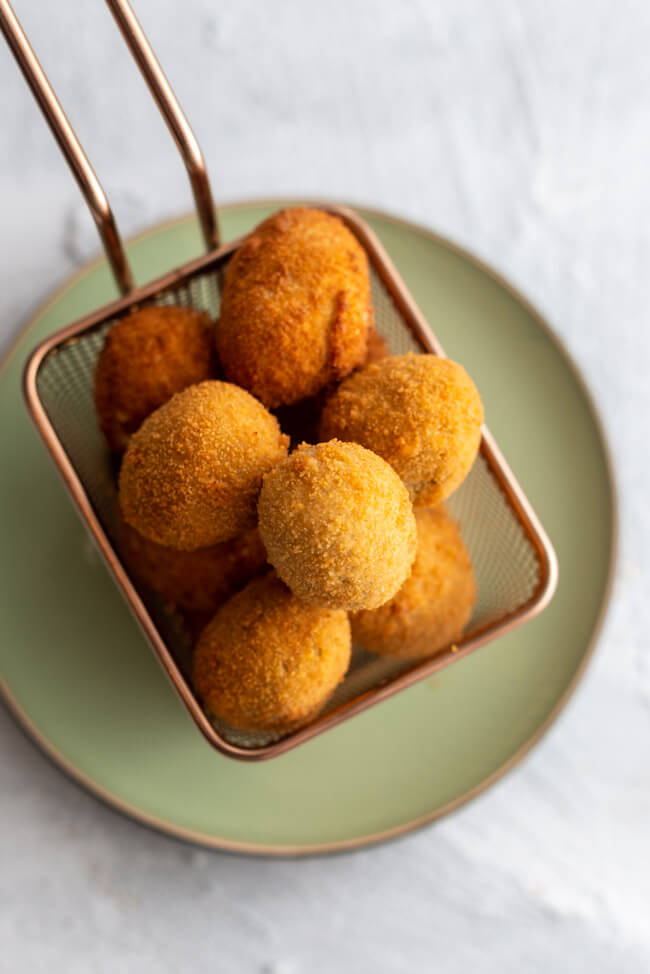 Originalrezept aus Kitchen Impossible: Olive Ascolane des Piceno - gefüllte und panierte Oliven in goldenem Körbchen auf hellem Untergrund.