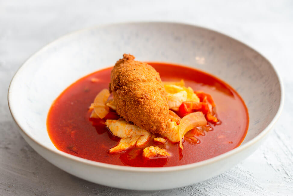 Originalrezept aus Kitchen Impossible: Pannonische Fischsuppe mit Fischklößchen in weißem Teller und hellem Untergrund.