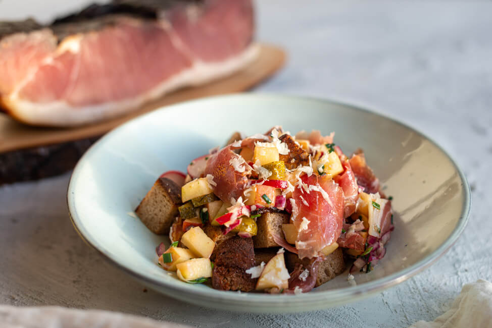 Brotsalat mit Schwarzwälder Schinken, Apfel und frischem Meerrettich in weißem Keramikteller.