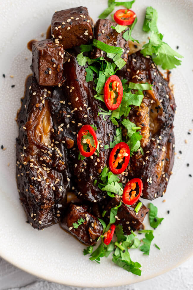 Chinesische Auberginen mit Tofu und Sesam auf hellem Porzellanteller und weißem Untergrund.