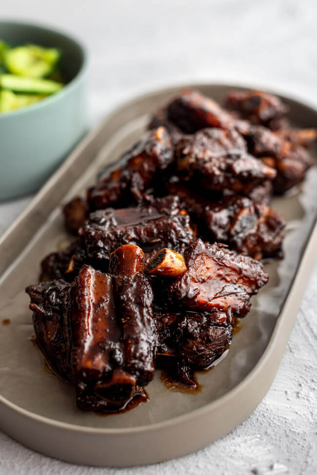 glasierte Chinesische Spare Ribs auf grauem Porzellanteller mit smashed cucumber salad in türkiser Porzellanschale auf hellem Untergrund.