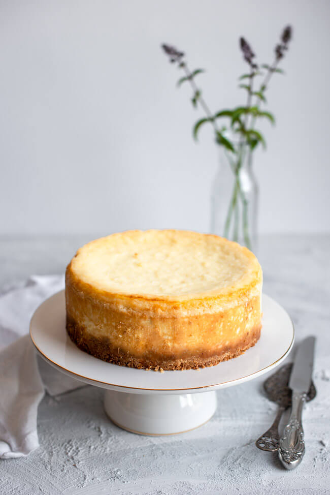 Kokos-Käsekuchen auf weißem Kuchenständer mit Goldrand und weißem Unter- und Hintergrund.