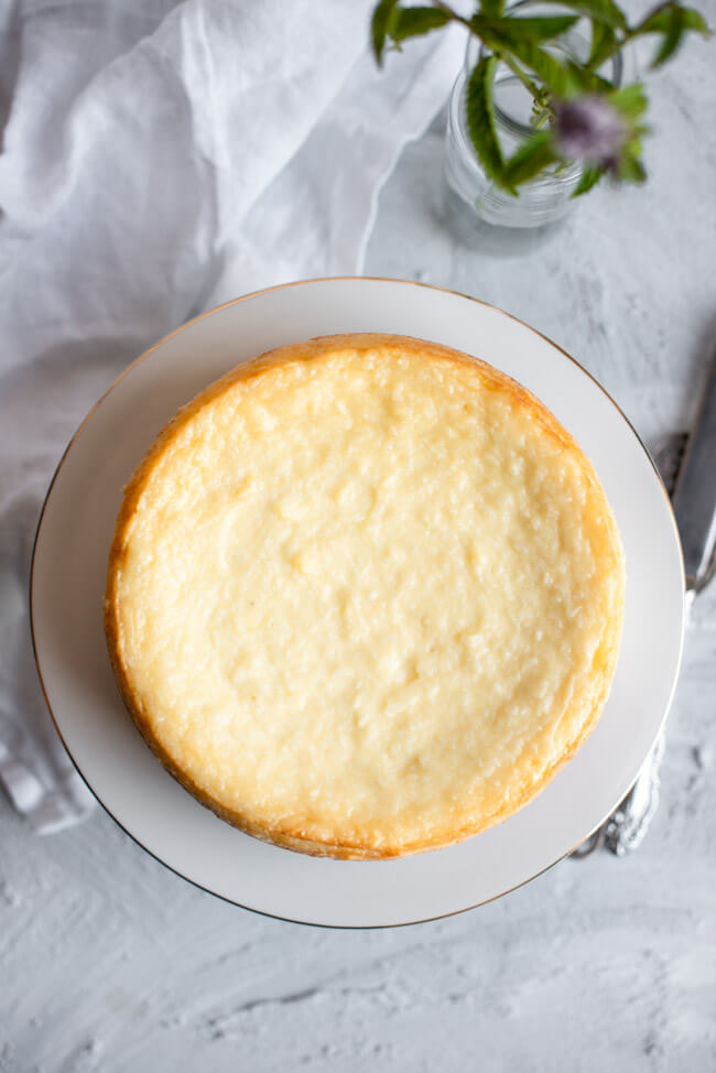 Kokos-Käsekuchen auf weißem Kuchenständer mit Goldrand und weißem Unter- und Hintergrund.