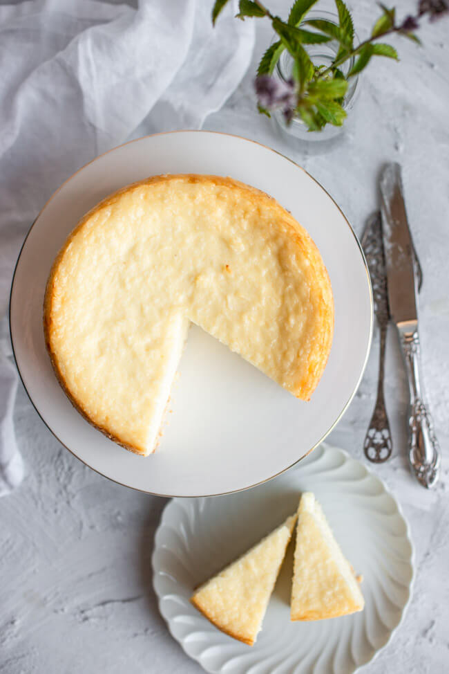 Kokos-Käsekuchen auf weißem Kuchenständer mit Goldrand und weißem Unter- und Hintergrund.