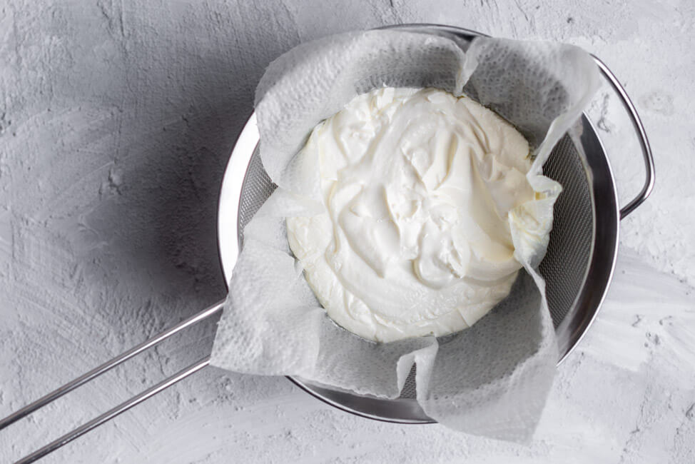 Joghurt in einem Sieb mit Küchenkrepp auf hellem Untergrund.