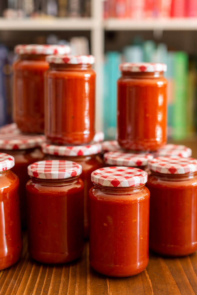 Tomatensauce in Gläsern eingeweckt auf Tisch mit Bücherregal im Hintergrund.