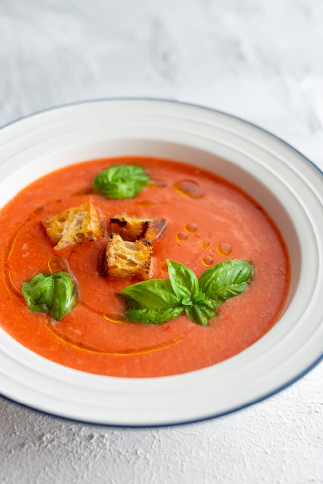 Wassermelonen Gazpacho mit Croutons und frischem Basilikum in weißem Teller mit blauem Rand.