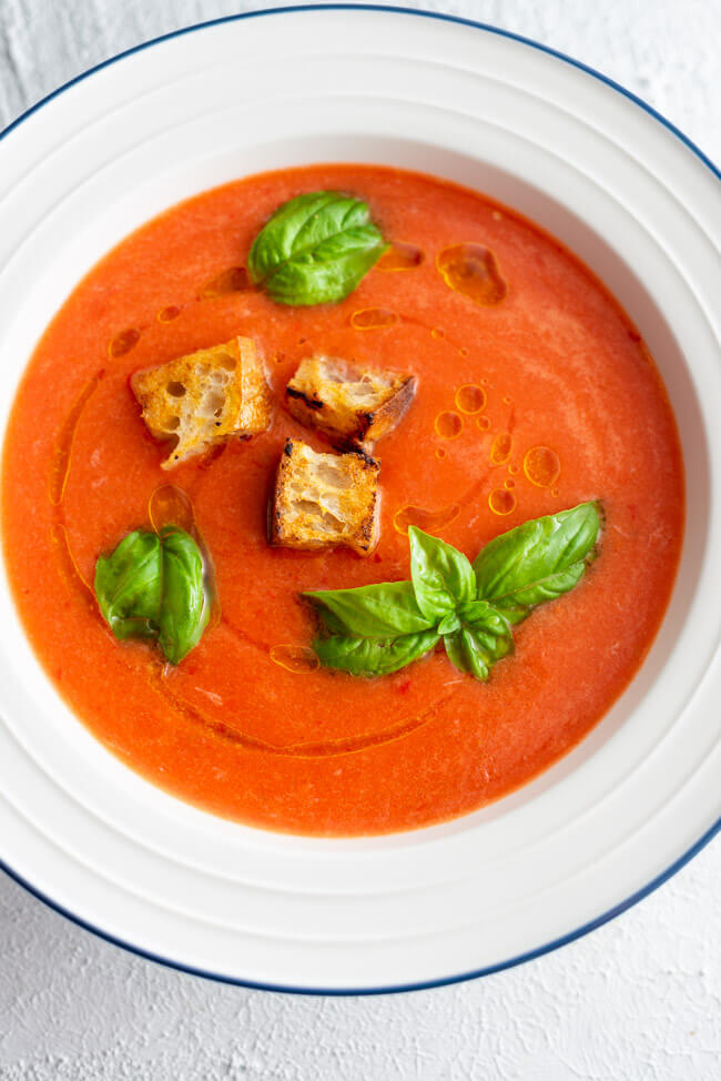 Wassermelonen Gazpacho mit Croutons und frischem Basilikum in weißem Teller mit blauem Rand.