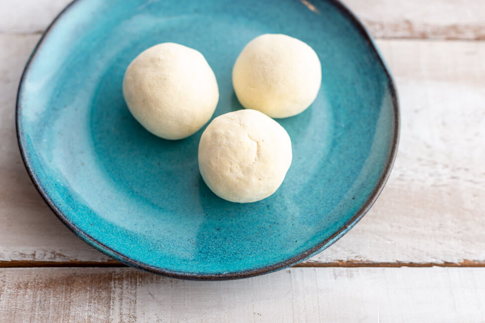 Zwetschgenknödel vor dem Kochen auf blauem Teller.