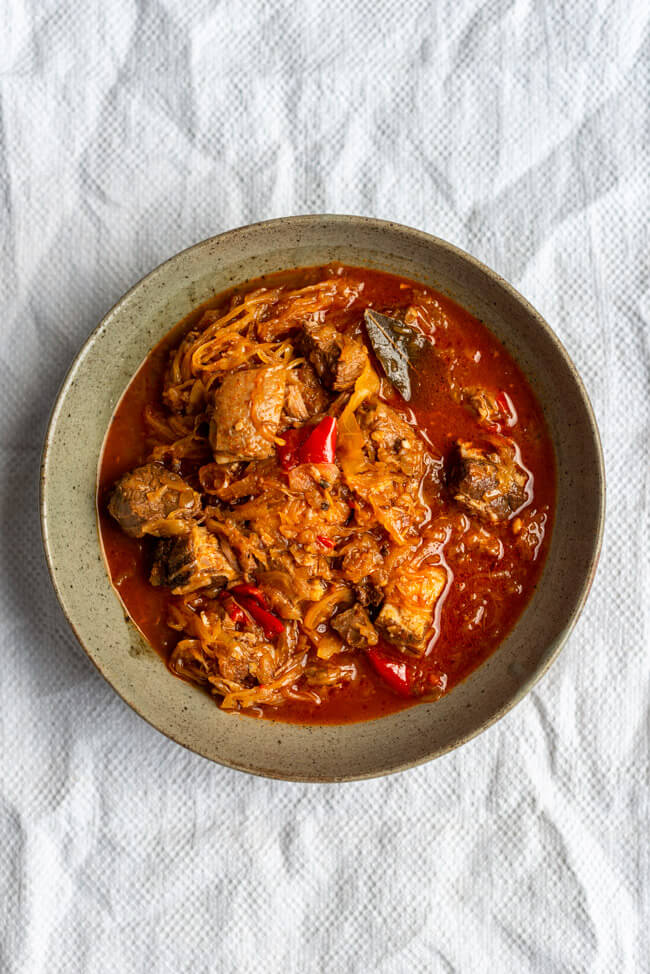 Szegediner Gulasch mit Sauerkraut in grauem Keramikteller auf weißer Tischdecke.