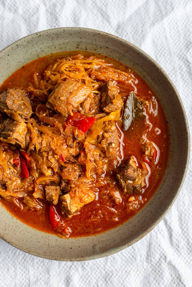 Szegediner Gulasch mit Sauerkraut in grauem Keramikteller auf weißer Tischdecke.