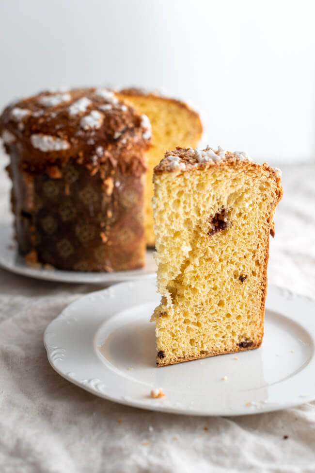 Aufgeschnittenere Panettone auf Kitchen Impossible auf weißem Teller und heller Tischdecke.