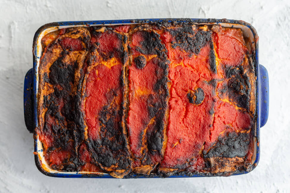 Melanzana alla Parmigiana, frisch aus dem Ofen in der Auflaufform und weißem Untergrund.