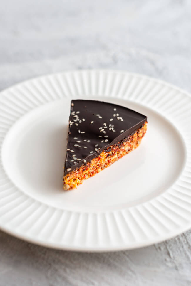 Ein Stück Power Cake, glasiert mit dunkler Schokolade, auf weißem Teller und hellem Untergrund.