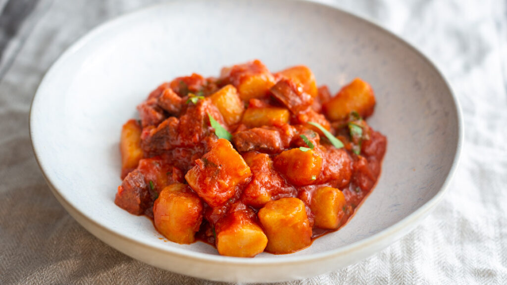 Gnocchi mit Sucuk Tomatensauce und Petersilie auf weißem Keramikteller und beigem Tischtuch.