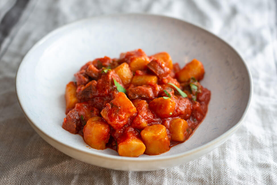 Gnocchi mit Sucuk Tomatensauce und Petersilie auf weißem Keramikteller und beigem Tischtuch.