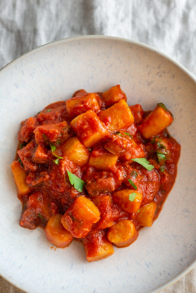 Gnocchi mit Sucuk Tomatensauce und Petersilie auf weißem Keramikteller und beigem Tischtuch.