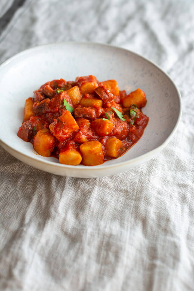 Gnocchi mit Sucuk Tomatensauce und Petersilie auf weißem Keramikteller und beigem Tischtuch.