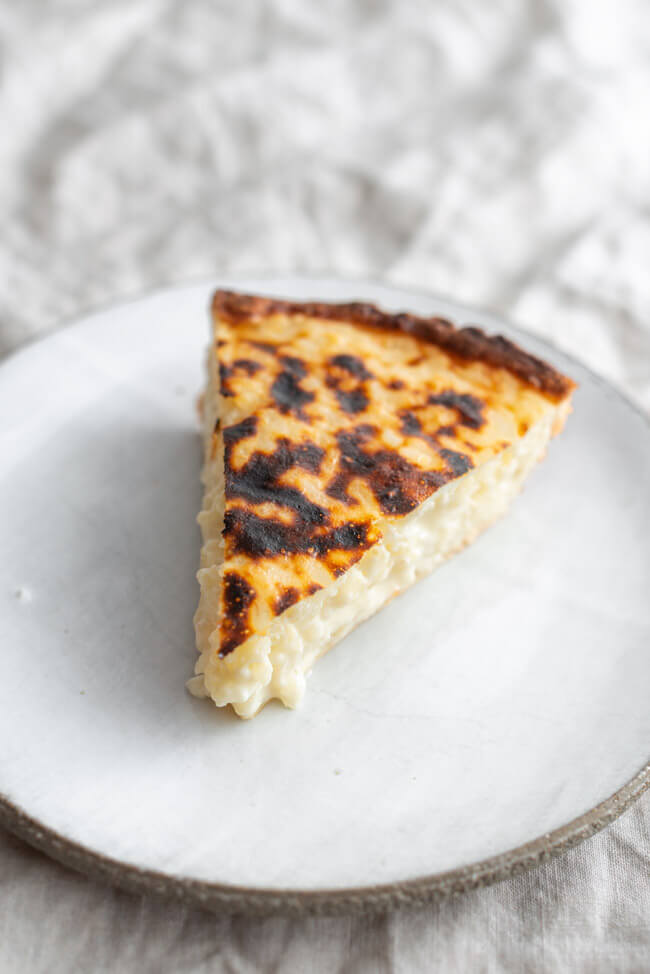 Ein Stück belgischer Milchreiskuchen auf hellem Keramikteller und beiger Tischdecke.