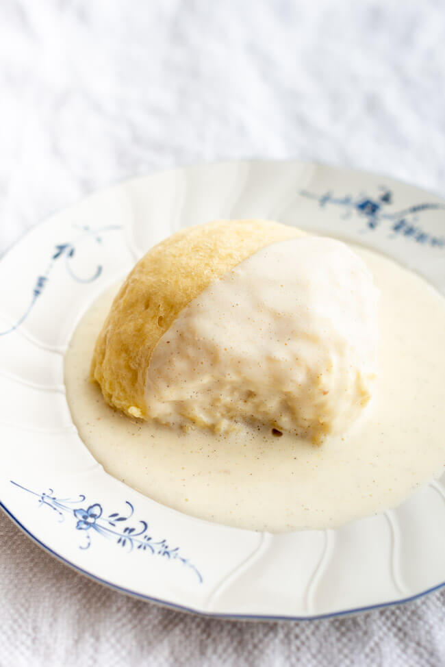Dampfnudel mit Vanillesoße auf weiß-blauem Porzellanteller auf weißer Tischdecke.