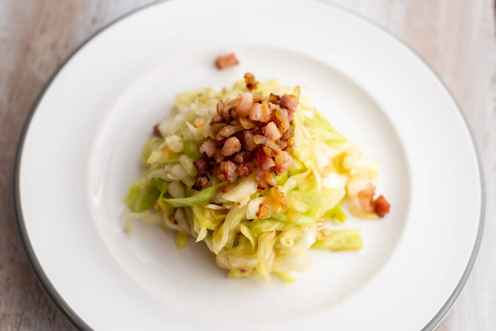 Krautsalat nach einem Rezept von Eckart Witzigmann auf weißem Porzellanteller und weißem Holztisch.
