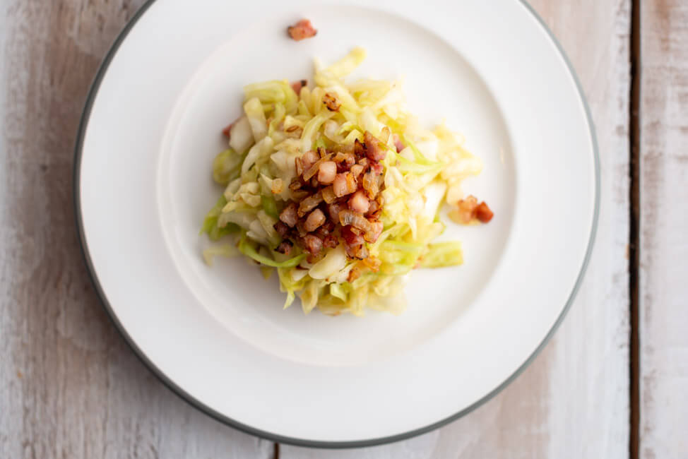 Krautsalat nach einem Rezept von Eckart Witzigmann auf weißem Porzellanteller und weißem Holztisch.