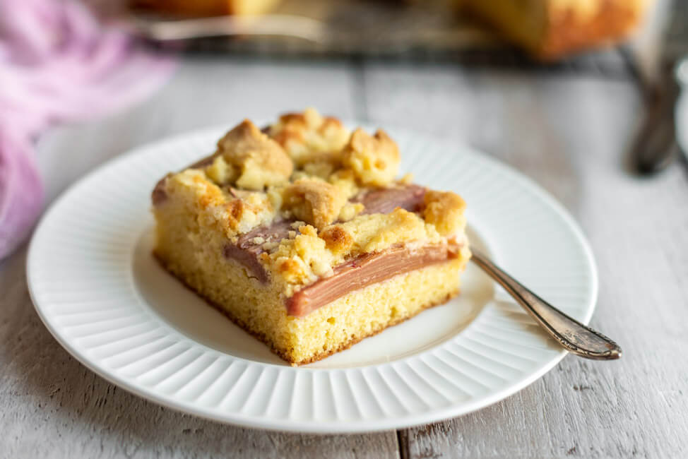 Ein Stück Rhabarber Streuselkuchen auf weißem Porzellanteller. #rhabarbersaison #rhabarber #rhabarberkuchen